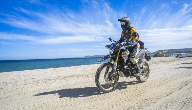 Piloto con equipo de seguridad completo manejando una ITALIKA DM300 en una playa de México.